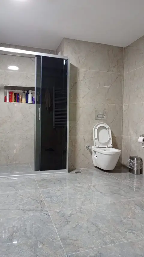Siyah camlı duşakabin, seramik kaplı niş ve asma klozetli banyo